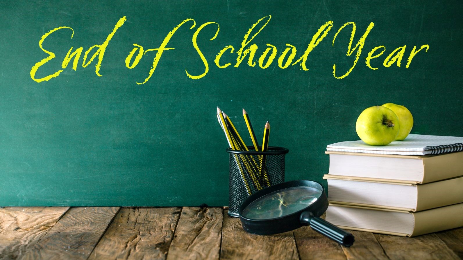 Green chalk board with the words "End of School Year" in Yellow chalk font, books, magnifying glass, pencils, and apples on a wood floor